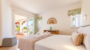 Habitación de hotel con cama, una mesita de noche con un jarrón verde, un adorno de pared y vistas al área exterior.