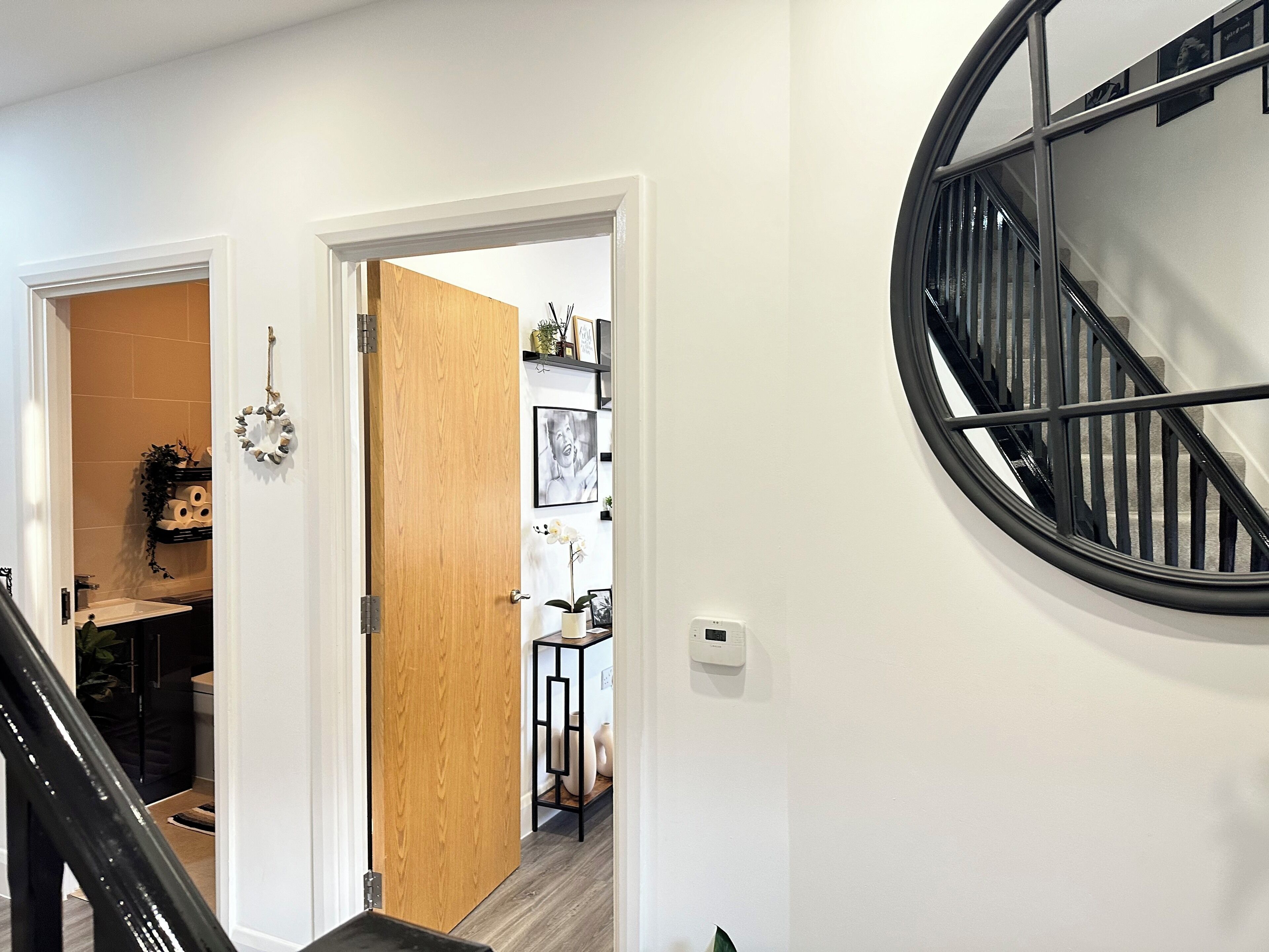 Un intérieur moderne avec une porte en bois donnant sur une salle de bain, un escalier noir et un thermostat fixé au mur.