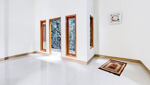 A spacious hallway with white walls, three wooden-framed windows, and a small rug on the floor. - Hotel O Homestay Putra Syariah (Kasihan)