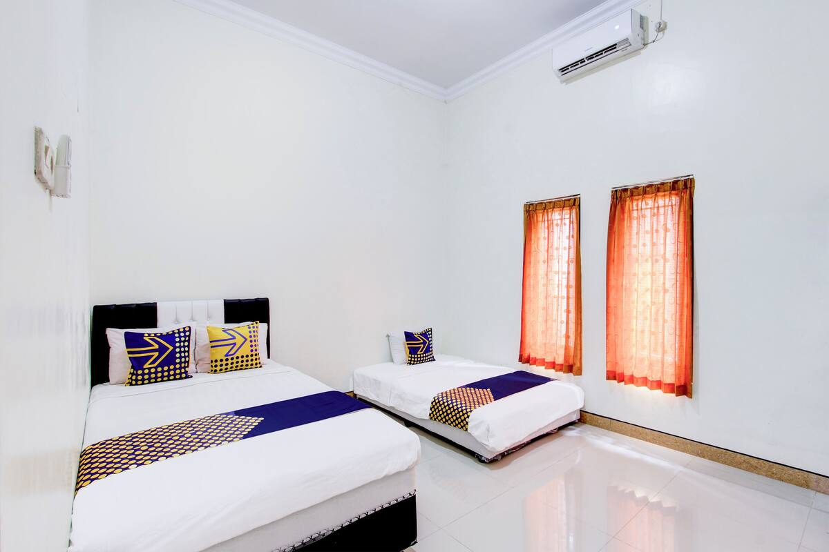 Habitación de hotel con dos camas, una pared blanca y un equipo de aire acondicionado.