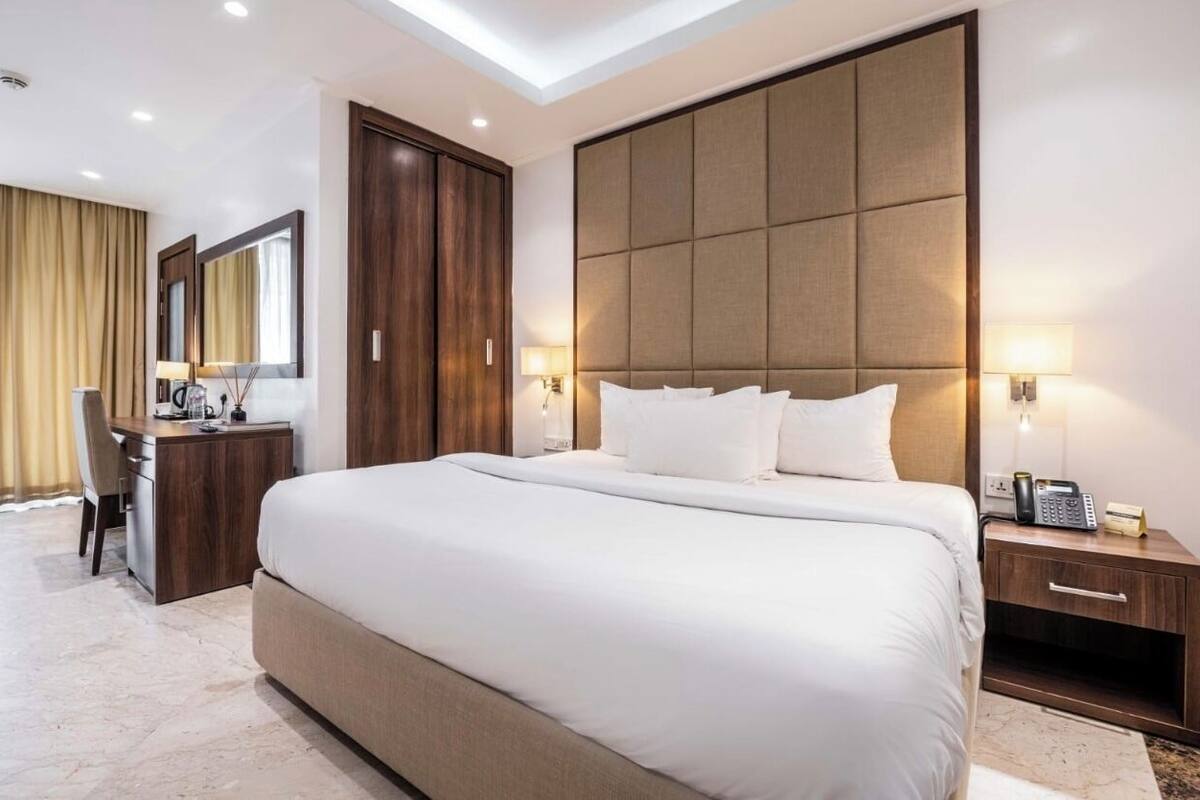 A modern hotel room with a large bed, a desk, a wardrobe, and a large mirror.