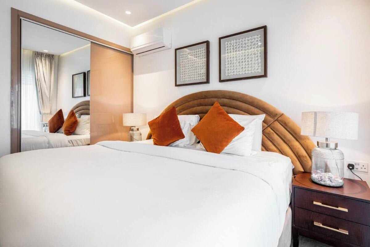 A modern hotel room with a large bed, a nightstand, a mirror, and framed artwork on the wall.