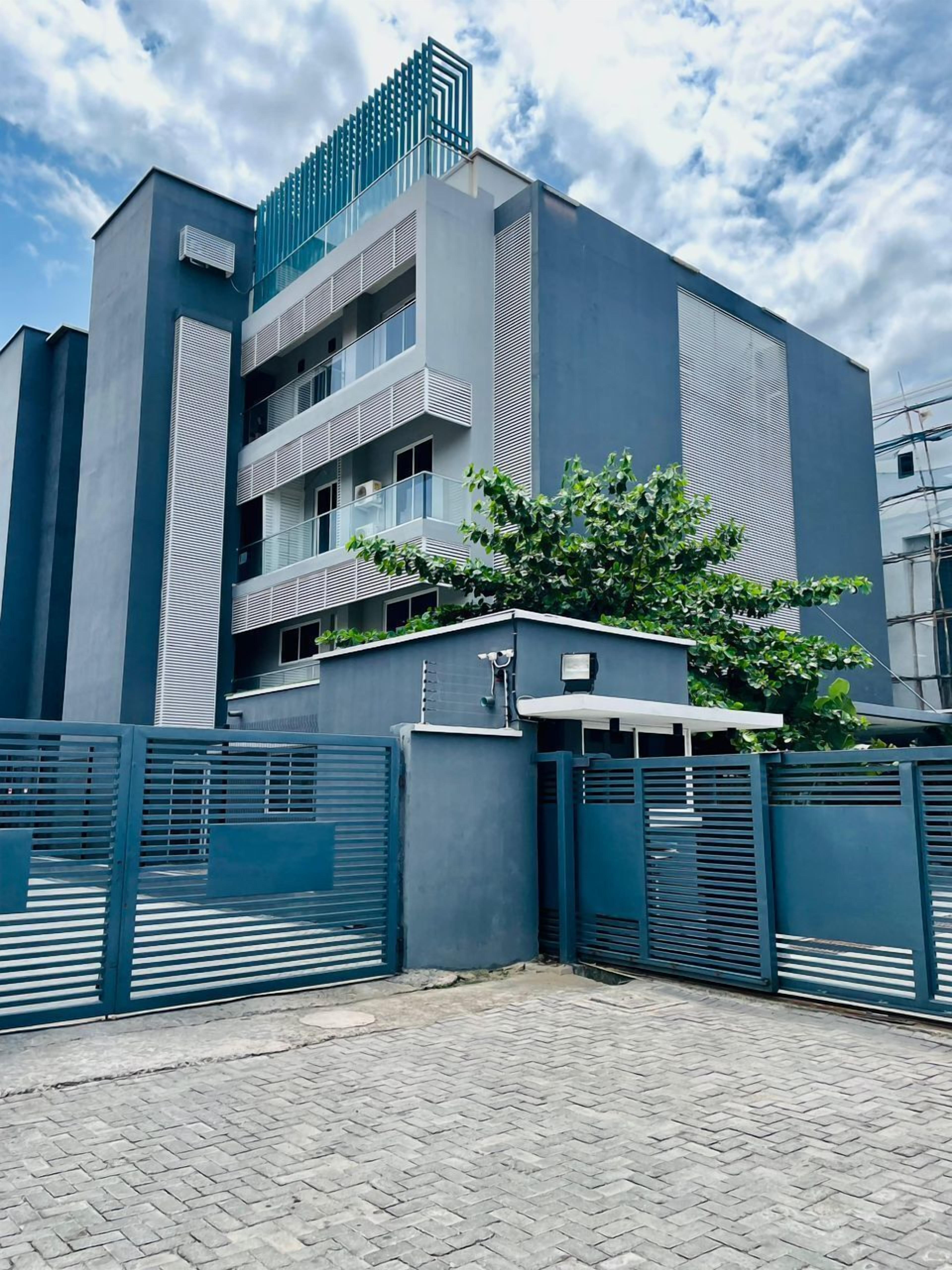 Un bâtiment moderne doté d’un toit plat, de nombreux balcons et d’une entrée sécurisée par un portail.