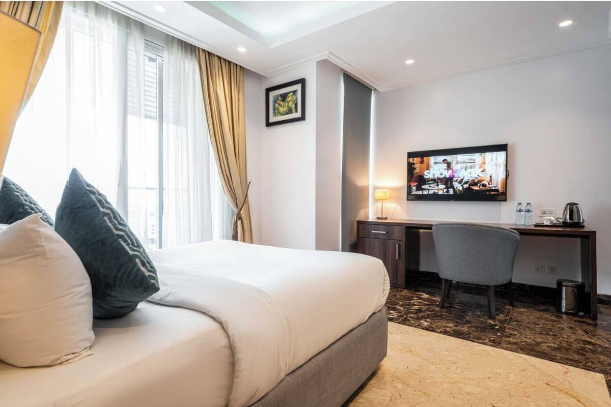A hotel room with a bed, a desk, a chair, a television, and a window with curtains.