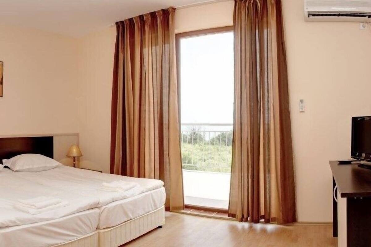 A hotel room with a bed, a desk with a computer, a lamp, and a window with curtains.