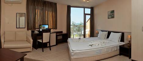Habitación de hotel con cama, escritorio, silla, televisor y balcón con vistas.