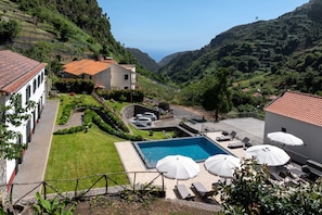 A pool area with lounge chairs and umbrellas, surrounded by a well-maintained lawn and a view of the valley. - Solar dos Reis by An Island Apart (Ribeira Brava)