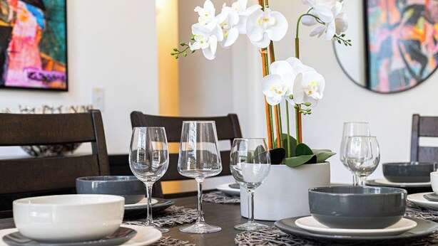A dining table set with white and gray bowls, wine glasses, and a potted orchid. - ⭐NEWLY REFURBISHED | 4 Bed Villa | Large Private Pool Deck | Minutes to Disney⭐ (Davenport)