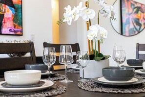 Une table à manger dressée avec des bols blancs et gris, des verres à vin et une orchidée en pot.