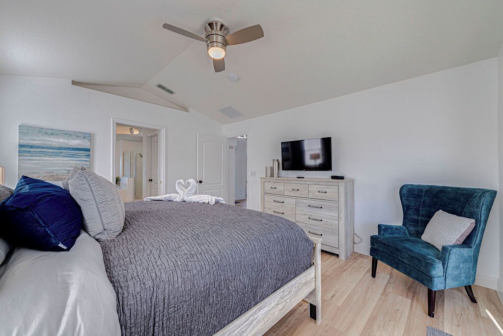 A bedroom with a bed, a TV, a chair, and a ceiling fan.