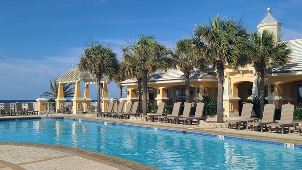A poolside area with lounge chairs and palm trees, a clear blue sky, and a building with a dome roof.