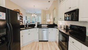 A modern kitchen with white cabinets, a black refrigerator, a dishwasher, a microwave, and a stove.