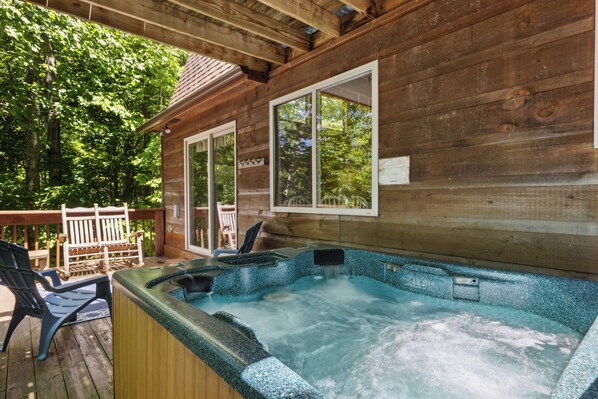 Une cabane en bois avec un jacuzzi sur une terrasse, entourée d’arbres.