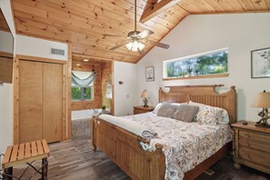 Une chambre à coucher avec un lit en bois, une table de chevet, une fenêtre donnant sur un beau paysage et un ventilateur de plafond.