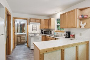 A kitchen with wooden cabinets, a white countertop, a refrigerator, a stove, and a microwave. - Cosy Cabin|King Suite main floor|Game Room|Hot Tub (Gatlinburg)