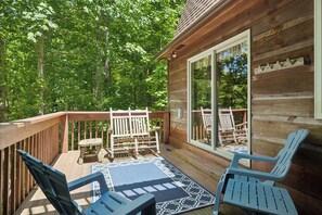 A wooden deck with a blue patterned rug, two blue Adirondack chairs, and a wooden bench. - Cosy Cabin|King Suite main floor|Game Room|Hot Tub (Gatlinburg)
