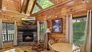 Ein gemütliches Blockhäuschen-Interieur mit Kamin aus Stein, Esstisch aus Holz und Stühlen.