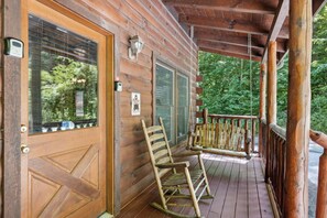 Une cabane en bois avec une véranda, une porte dotée d’une fenêtre et une enseigne accrochée au mur.