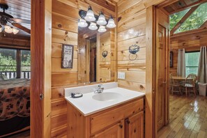L’intérieur d’une cabane en bois, avec un évier blanc, des armoires en bois, un miroir et un ventilateur de plafond.