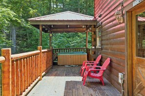 Une terrasse en bois avec un jacuzzi, deux chaises rouges et un espace abrité doté d’une rambarde.