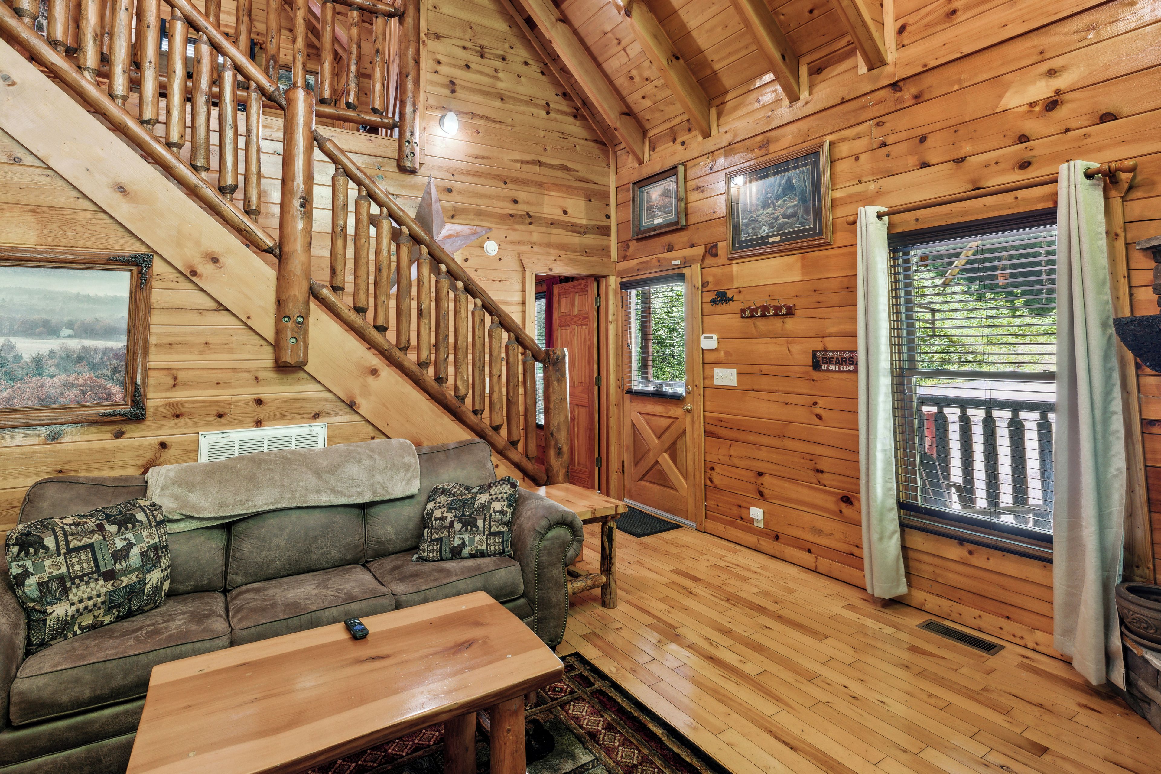 Ein Interieur einer Holzhütte mit einer Holztreppe, einer Couch mit gemusterten Kissen, einem Holztisch und einer Tür mit einem Schild.