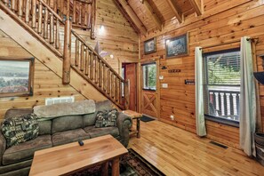 L’intérieur d’une cabane avec un escalier en bois, un canapé agrémenté de coussins à motifs, une table en bois et une porte avec une pancarte.