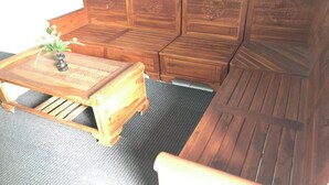 Een houten bank met ingewikkelde houtsnijwerken, een kleine houten tafel met een vaas, en een vloermat.