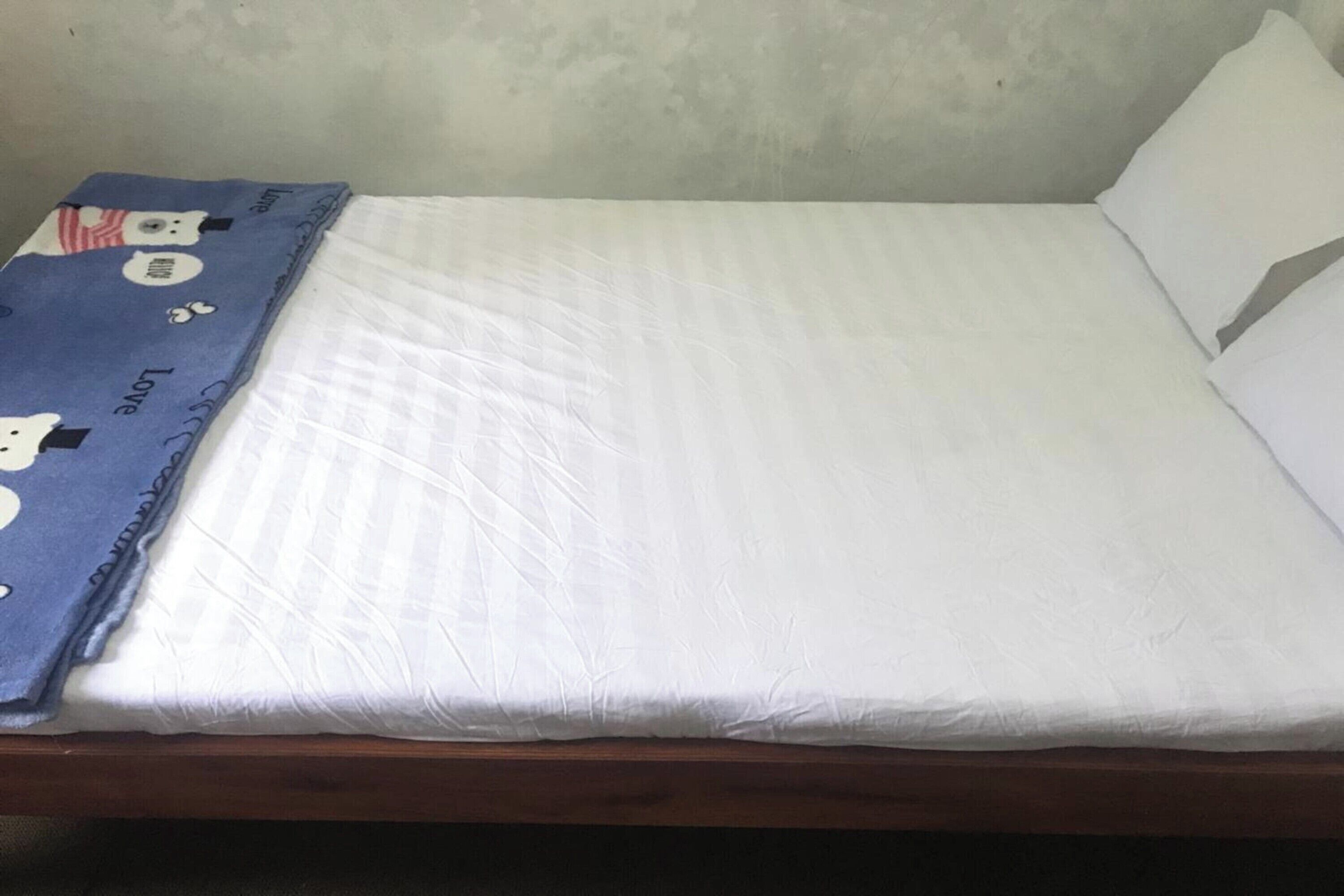 A single bed with a white mattress and a blue blanket with cartoon characters.