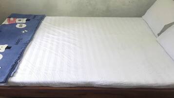 Una cama individual con colchón blanco y manta azul con personajes de dibujos animados.