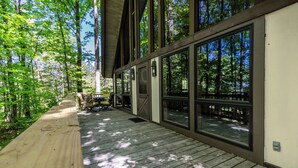 A wooden deck with large windows overlooking a forested area. - Woodland Lodge - Perfect Family Ski Chalet! Close to Nubs Nob & Boyne! (Harbor Springs)