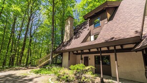 A rustic cabin with a sloped roof, wooden exterior, and a stone pathway leading to the entrance. - Woodland Lodge - Perfect Family Ski Chalet! Close to Nubs Nob & Boyne! (Harbor Springs)