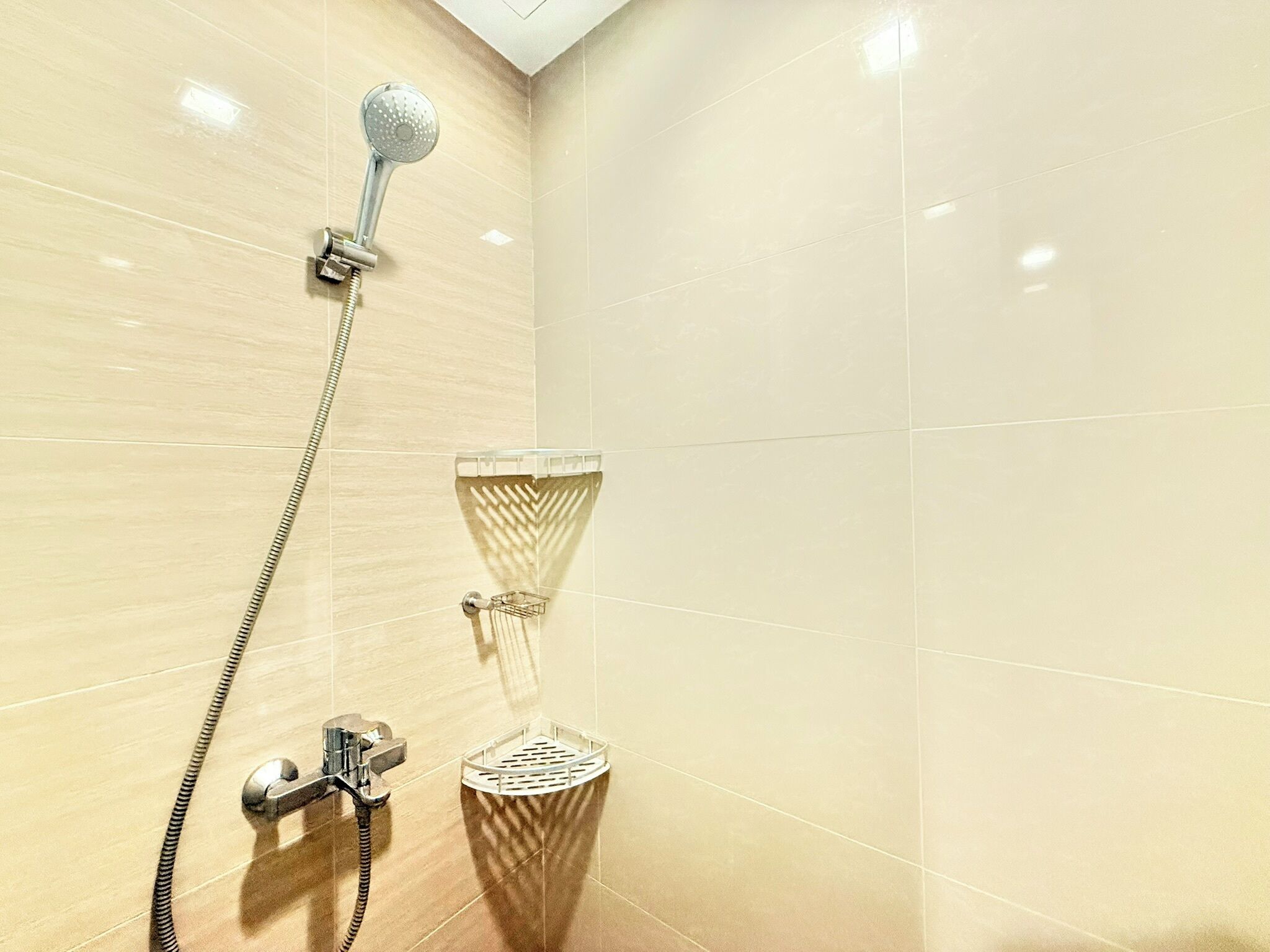 A shower with a handheld showerhead, a wall-mounted faucet, and a glass-enclosed showerhead.