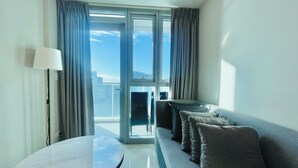 Una habitación de hotel moderna con balcón, una mesa redonda, un sofá con cojines y una lámpara.