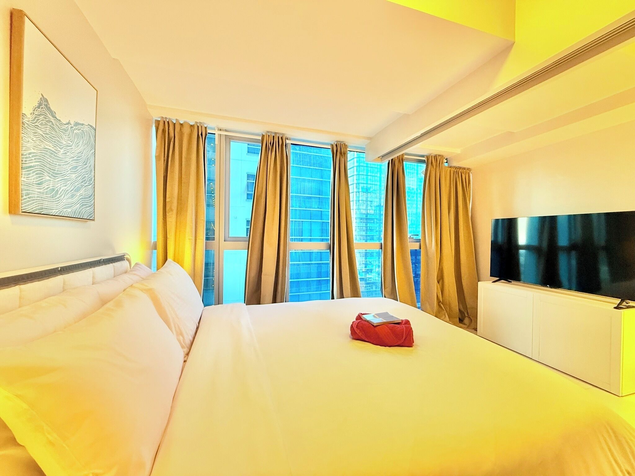 A hotel room with a bed, a flat-screen TV, a window with curtains, and a painting on the wall.