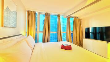 A hotel room with a bed, a flat-screen TV, a window with curtains, and a painting on the wall.