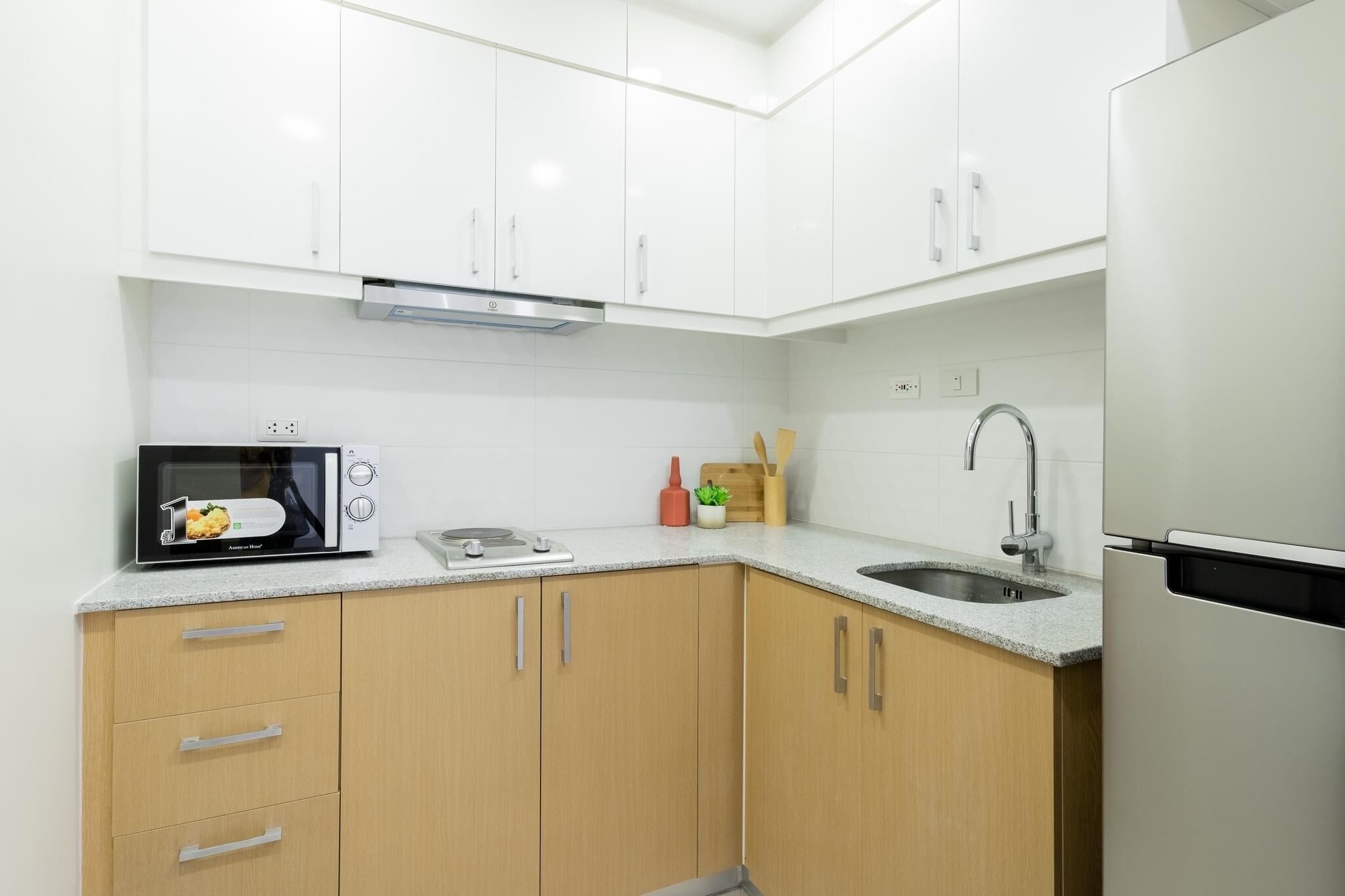 A modern kitchen with white cabinets, a microwave, a sink, and a refrigerator.