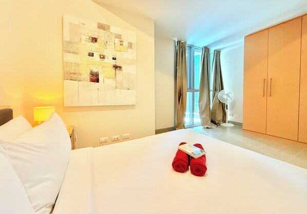 A hotel room with a neatly made bed, a wall art piece, a window with curtains, and a wardrobe.