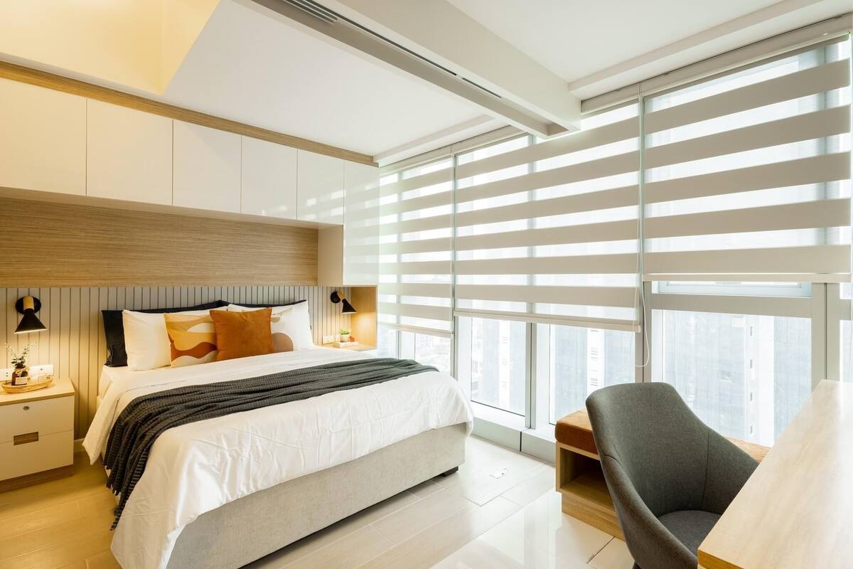 A modern bedroom with a large bed, bedside tables, a chair, and a view through floor-to-ceiling windows.