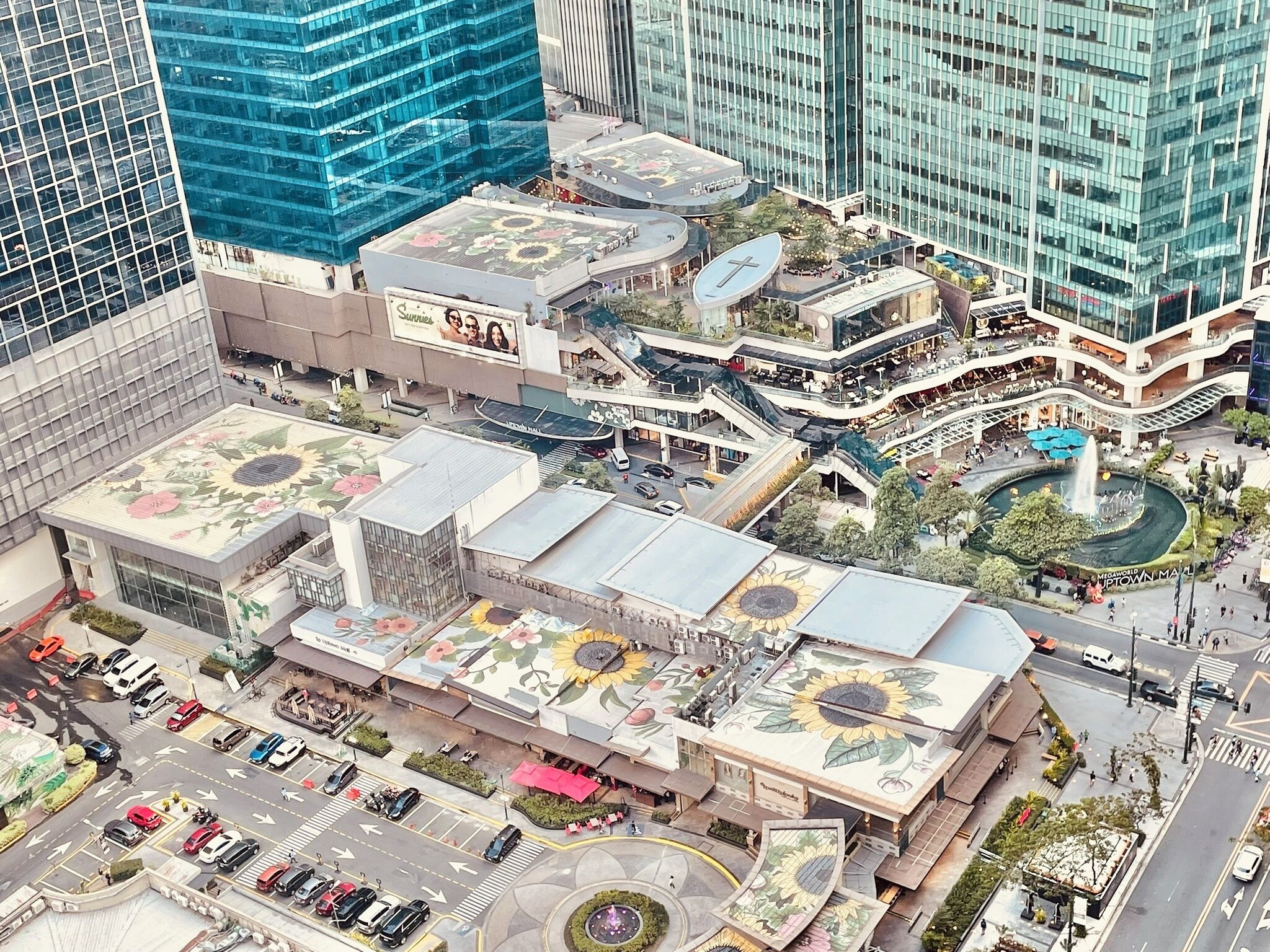 Un edificio moderno con jardín en la azotea, una fuente central y un centro comercial.