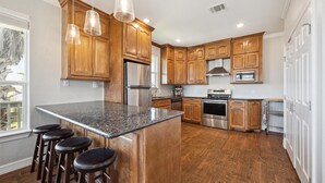 A modern kitchen with wooden cabinets, stainless steel appliances, and a central island with bar stools. - Surfside Retreat - Great Views & Steps from Beach (Freeport)