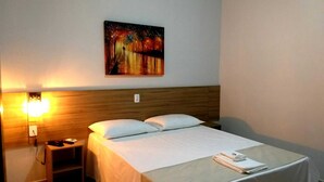 A hotel room with a bed, nightstand, and a painting on the wall.