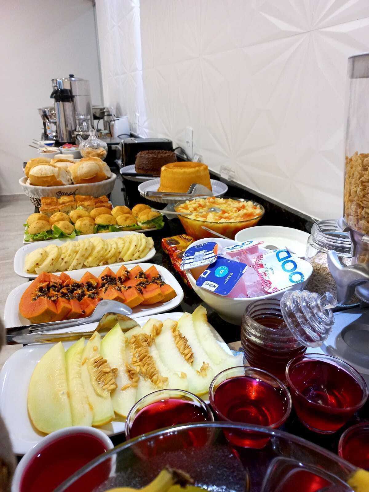 En buffet med forskellige spiser, herunder brød, kager, frugt og drikkevarer.