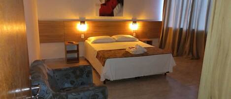 Ein Hotelzimmer mit Bett, Nachttischen, einem Sessel und einer Wandleuchte.