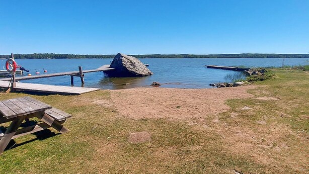 Järvenrantainen piknikalue, jossa on puinen laituri, suuri kalliomuodostelma ja pelastusrengas.