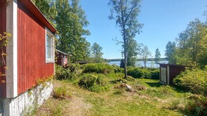 Punainen rakennus, jossa on ikkuna, ja sen ympärillä on vehreää kasvillisuutta ja kirkas taivas.