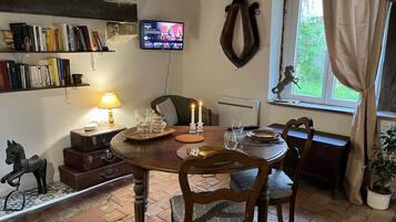 A cozy dining area with a wooden table, chairs, a television mounted on the wall, and a bookshelf filled with books.