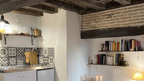 Une cuisine rustique avec des poutres apparentes, un dosseret carrelé et un coin repas avec une table ronde prévue pour quatre personnes.