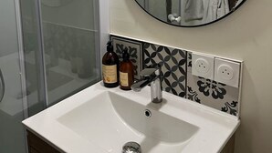 Une salle de bain avec un lavabo blanc, un miroir rond et deux bouteilles de shampoing.
