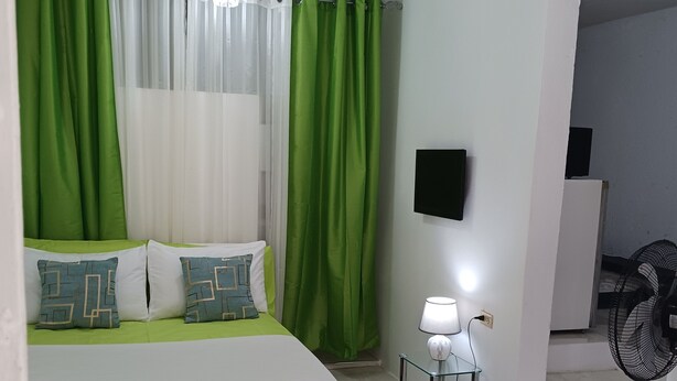 A bedroom with a bed, green curtains, a TV, a lamp, and a fan.