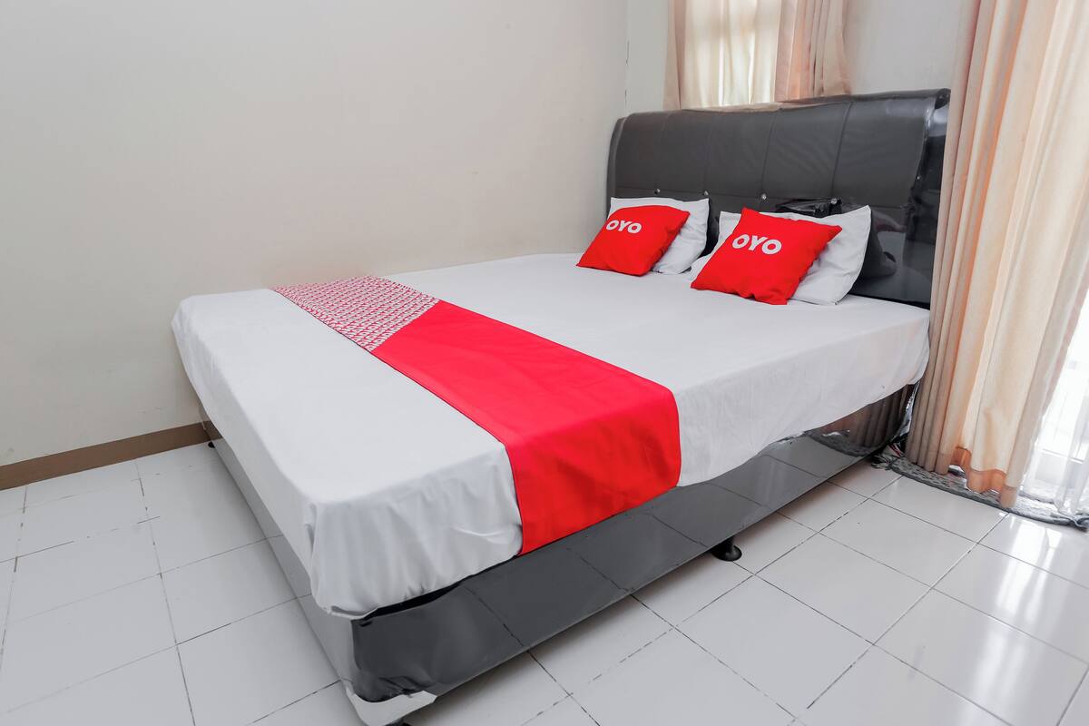 A bed with a white and red bedspread, two red pillows with "OYO" branding, and a grey headboard.